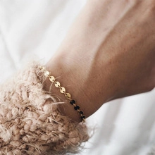Detail of minimalist gold chain bracelet worn over a cozy knitted sleeve