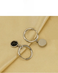 Détail de boucles d'oreilles asymétriques en acier avec pierre noire sur soie dorée