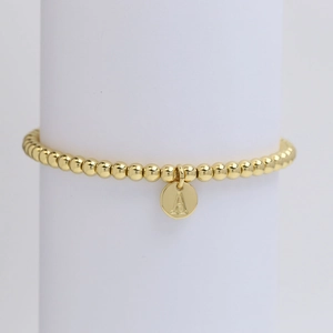 Close-up of golden beaded bracelet featuring a round letter A pendant on a white stand