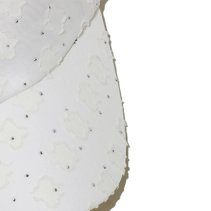 Detailansicht einer weißen Baseballkappe mit floralen Texturen und Strassstein-Akzenten