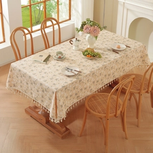 Detailed view of beige floral tablecloth with delicate fringes on a wooden dining table