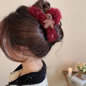 Close-up of a burgundy plush hair claw clip with a cute bear toy on a model hairstyle