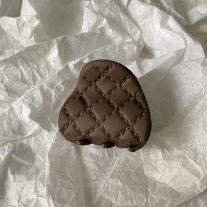 Close-up of a brown matte hair claw clip with a quilted pattern on a white paper background