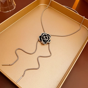 Detailed close-up of a black camellia necklace pendant on a golden metallic tray