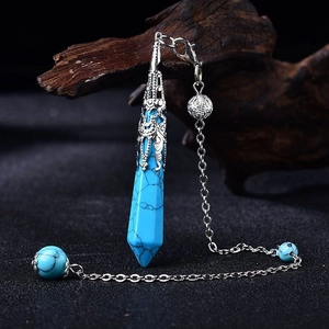 Detail of blue turquoise hexagonal pendulum with ornate silver cap on rustic wood