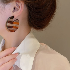 Detail of a large striped resin hoop earring worn by a model in a warm brown and orange tone