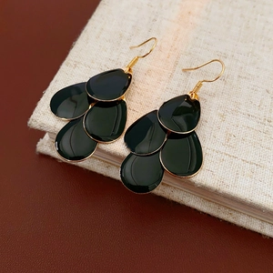 Detailed view of layered black teardrop earrings with gold edges on a book surface