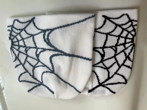 Flat lay of two knitted beanies featuring a dark blue spider web pattern on white fabric