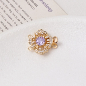 Macro detail of 14K gold flower clasp with purple gemstone and cubic zirconia