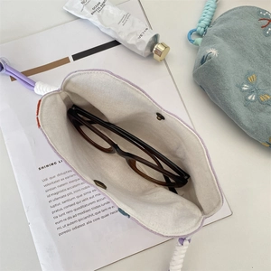 Gros plan d'une pochette à lunettes en lin brodé avec poignée tressée et doublure