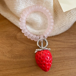 Détail d'un élastique spirale rose avec un pendentif fraise en peluche rouge vif