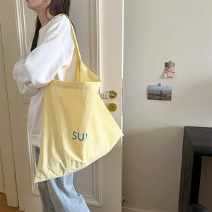 Detail of the light yellow large capacity tote bag featuring blue SUN letter print