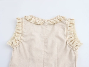 Détail des franges sur le col en V d'une robe bohème sans manches beige