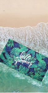 Detail of soft quick-dry beach towel with tropical leaves print on a sandy beach