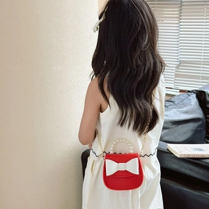 Red children crossbody bag with pearl handle and bow detail worn by a child