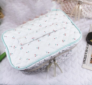 Detailed view of quilted cherry print makeup bag with blue trim and ribbon zippers
