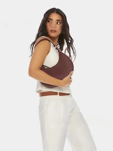 Close-up of a stylish burgundy leather crescent-shaped shoulder bag worn by a model