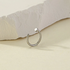 Macro shot of silver C-shaped non-piercing nose ring on a minimalist stone background