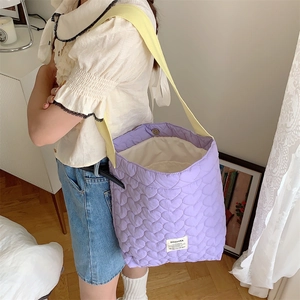 Detail of purple heart-quilted shoulder bag with magnetic snap and wide yellow strap