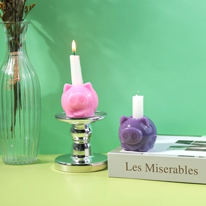 Détail des bougeoirs cochon rose et violet avec des bougies piliers allumées
