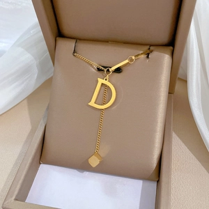 Close-up of golden letter D pendant and cube charm necklace in a beige jewelry box