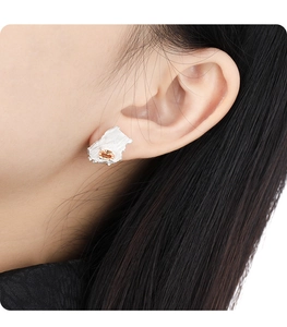 Close-up of asymmetric silver stud earring with textured surface and yellow gemstone