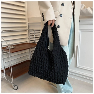 Close-up of black pleated tote bag with bubble texture held by a model in a blazer