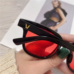 Close-up of black glossy sunglasses frame with a distinctive golden V-shaped logo detail