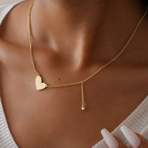 Macro detail of golden hammered heart pendant necklace worn over white knitwear