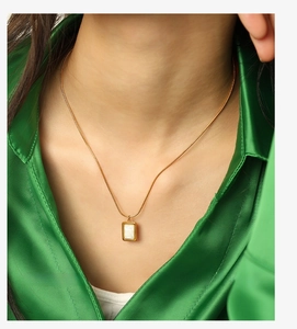 Gros plan du collier doré avec pendentif rectangulaire en nacre sur soie verte