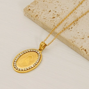 Macro shot of oval gold necklace pendant with Virgin Mary engraving and crystal border