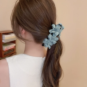 Détail d'une élégante pince à cheveux fleurie en tissu bleu-gris portée sur un chignon chic
