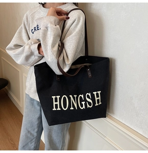 Detail of black canvas tote bag with brown leather straps and white HONGSH print