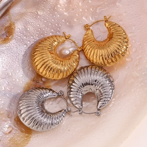 Macro detail of gold and silver textured hoop earrings with ribbed horn pattern on watery surface