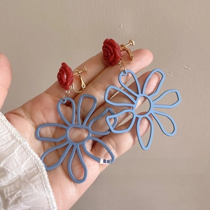 Detail of red rose and blue hollow flower earrings with gold metal clips on hand