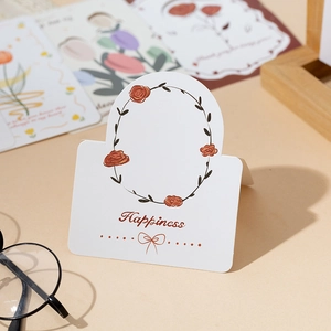 Macro shot of a white paper greeting card with a brown rose wreath and Happiness text