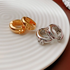 Macro detail of gold and silver metallic hoop earrings with B-letter design on ceramic