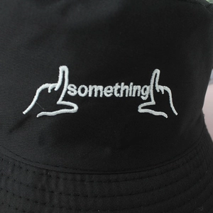 Detailed close-up of white 'something' embroidery on a black cotton canvas bucket hat