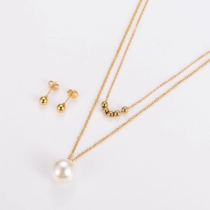 Détail d'un collier double épaisseur doré avec perle blanche et boucles d'oreilles clous