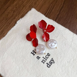 Close-up of red flower petal earrings with white baroque pearl drops on art paper