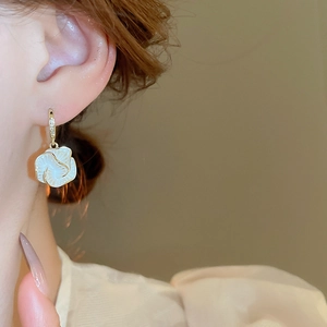 Close-up of white camellia drop earring with gold trim and zircon on woman ear