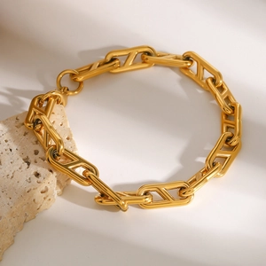 Close-up of golden geometric H-link chain bracelet draped over a light-colored stone