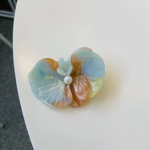 Elegant floral petal hair clip with colorful resin and pearl center on white surface