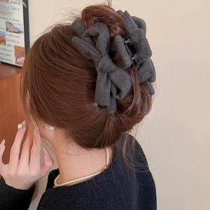 Detailed view of a dark grey fabric bow claw clip on styled hair for elegant hairstyling