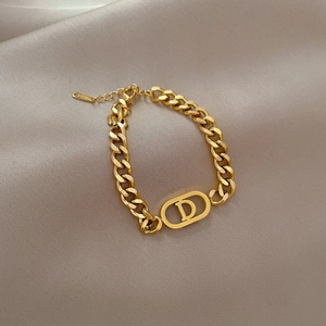Détail d'un bracelet à grosse chaîne dorée avec pendentif D sur soie couleur champagne