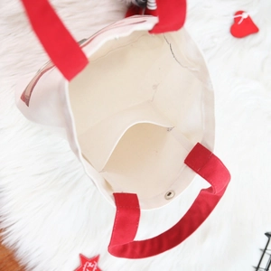 White canvas Christmas gift bag with red handles and metal magnetic closure on plush background