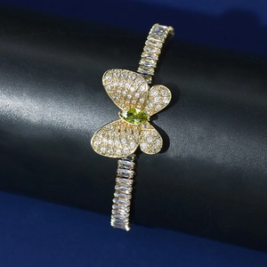 Detailed shot of golden butterfly bracelet with white zircons and olive green stone