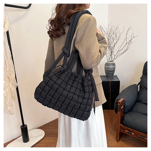 Quilted black puffer tote bag shown on model wearing brown blazer and white skirt