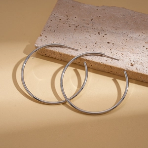Polished silver hoop earrings displayed on a textured stone with natural shadows