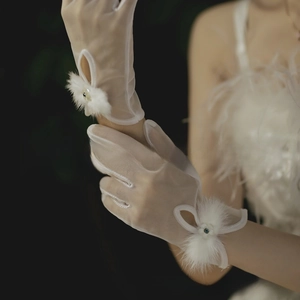 Close-up of white sheer bridal gloves featuring plush pom-poms and pearl accents